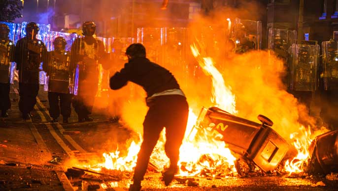 Southport, Merseyside, Royaume-Uni, le 30 juillet 2024, un émeutier jette des briques sur la ligne de police au-dessus du feu.